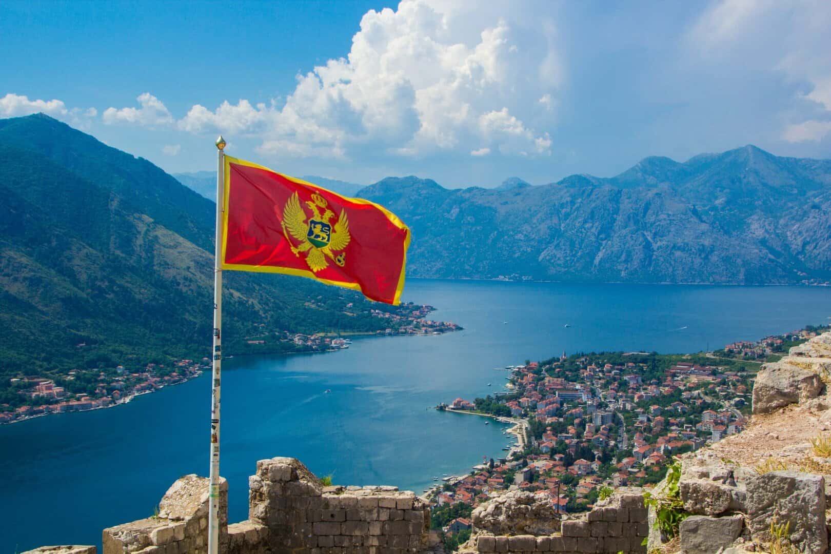 View from above on the Kotor and Bay of Kotor, Montenegro. Waving in the wind flag of Montenegro on Ancient fortress wall above Kotor.