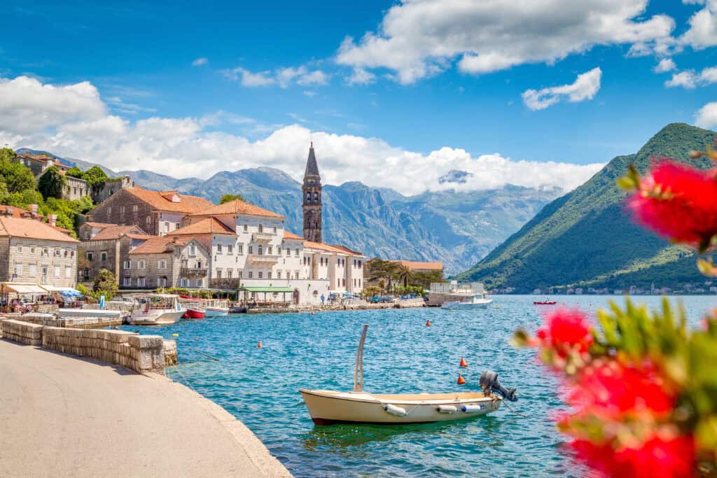 Scenic panorama view of the historic town of Perast at famous Bay of Kotor with blooming flowers on a beautiful sunny day with blue sky and clouds in summer, Montenegro, southern Europe